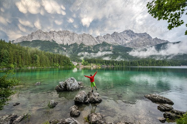 Young man sticks his arms in the air and stands on a rock on the shore