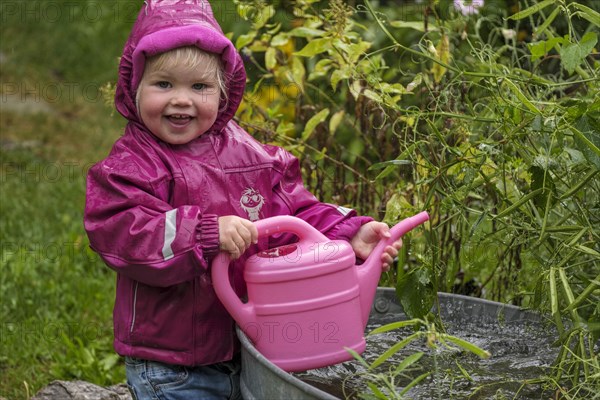 Little girl with rubber boots and rain jacket playing with water and watering can in the rain