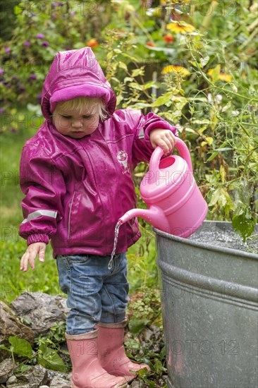 Little girl with rubber boots and rain jacket playing with water and watering can in the rain