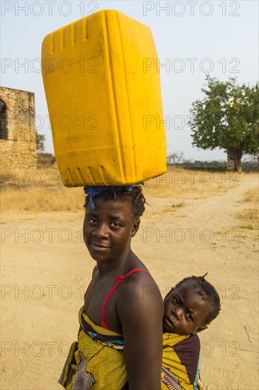 Woman with her baby on the back carrying a water canister on her head