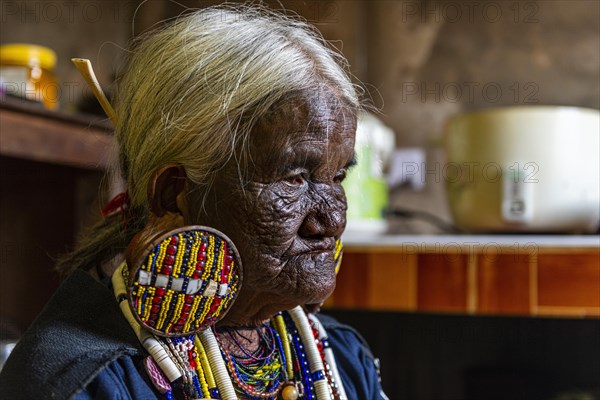 Chin Kaang hill-tribe woman with traditional facial tattoo and elaborate tribal earrings playing a flute with her nose