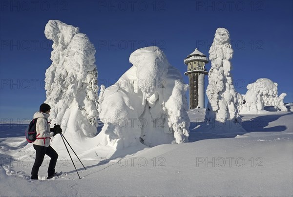 Snowshoe runner looking at winter landscape with snow-covered fir trees and Feldberg tower
