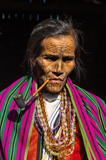 Chin woman with spiderweb tattoo smoking a pipe