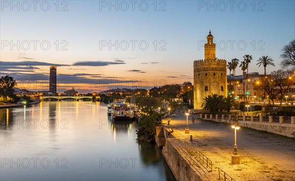 Boardwalk at the river Rio Guadalquivir with illuminated Torre del Oro