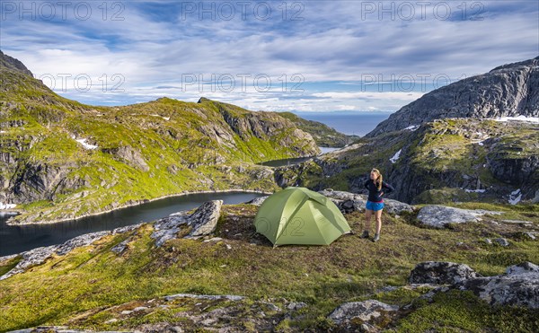 Hiker stands next to tent in the mountains