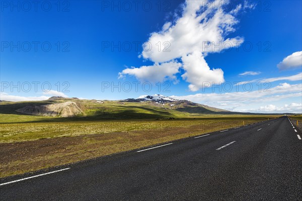 Asphalt road through barren volcanic landscape with view of snow-capped volcano Snaefellsjoekull