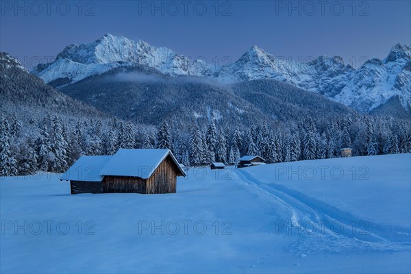 Winterly hummock meadows with hay barn and Karwendel mountains at dusk