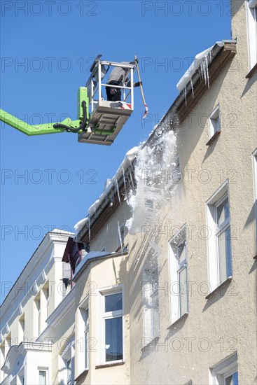 Man in lift knocks icicles off a gutter