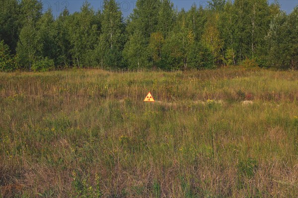 Warning sign against radioactive radiation in meadow