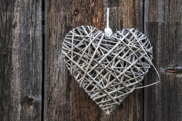 Woven heart hanging on an old wooden facade made of weathered wood