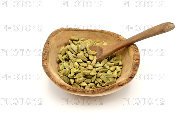Cardamom pods in a wooden rustic bowl with a wooden spoon against a white background