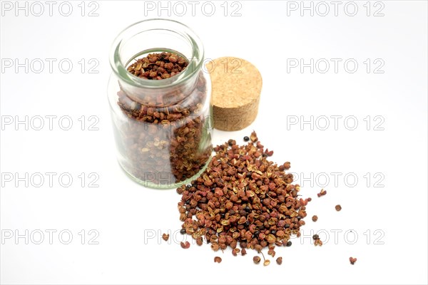 Sichuan peppercorns beside and in a 150ml glass spice jar against a white background