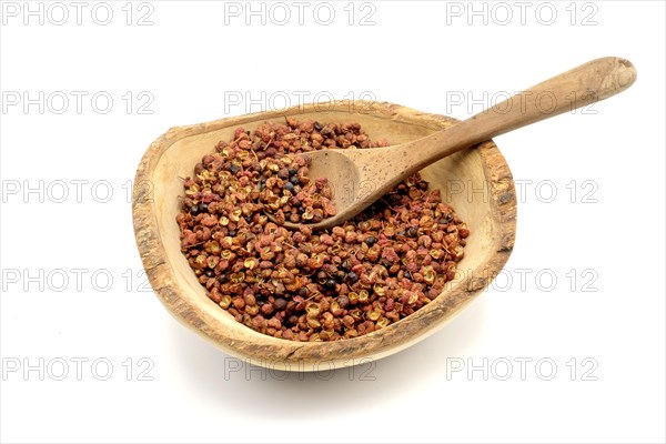 Sichuan peppercorns in a wooden rustic bowl with a wooden spoon against a white background