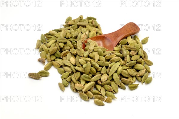 A pile of cardamom pods with a wooden spoon against a white background