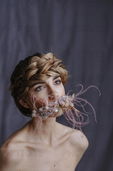 Young woman with flower wreath in front of mouth