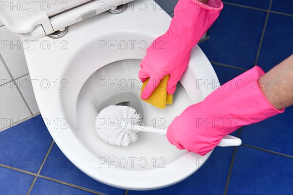 Person with rubber gloves cleans toilet with brush