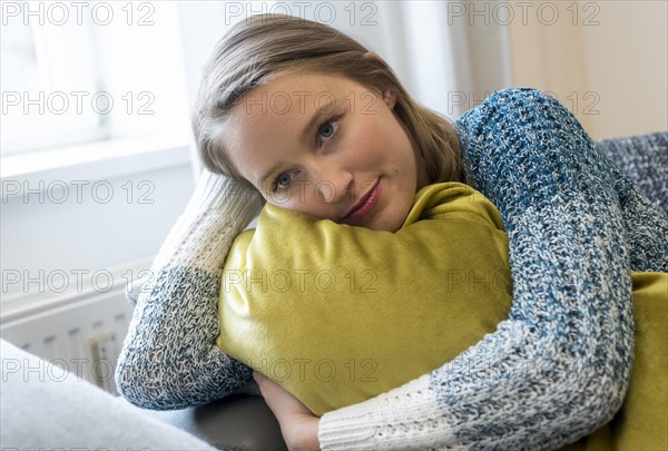 A young woman lies on a sofa with a big pillow