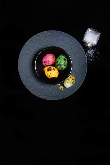 Coloured quail eggs in small bowls and salt shaker