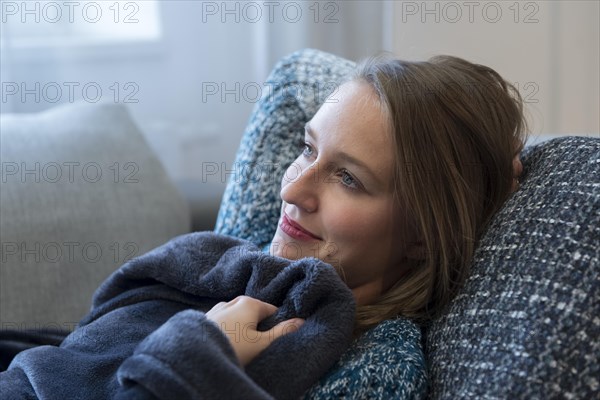 A young woman lies cuddled up in a blanket on a sofa in Dorfen