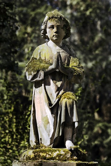 Praying grave sculpture with moss at Melaten cemetery