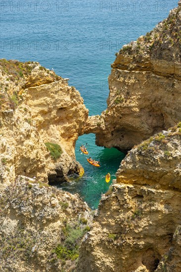 Three kayaks in the turquoise sea sailing through rock arches