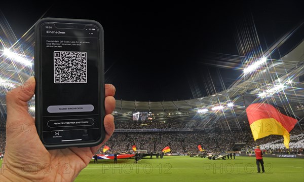 Hand holds smartphone with Luca app for digital contact tracking in packed football stadium