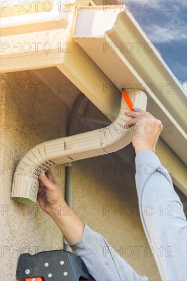 Worker attaching aluminum rain gutter and down spout to fascia of house