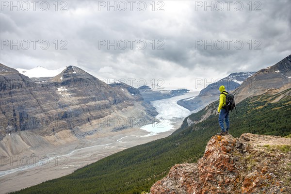 Hiker standing on rocks overlooking valley with glacier tongue