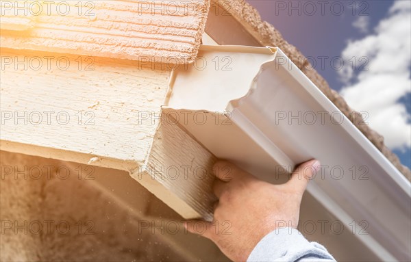 Worker attaching aluminum rain gutter to fascia of house