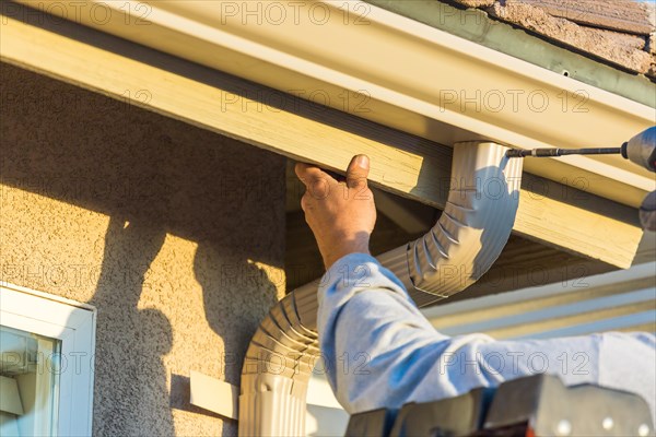 Worker attaching aluminum rain gutter and down spout to fascia of house