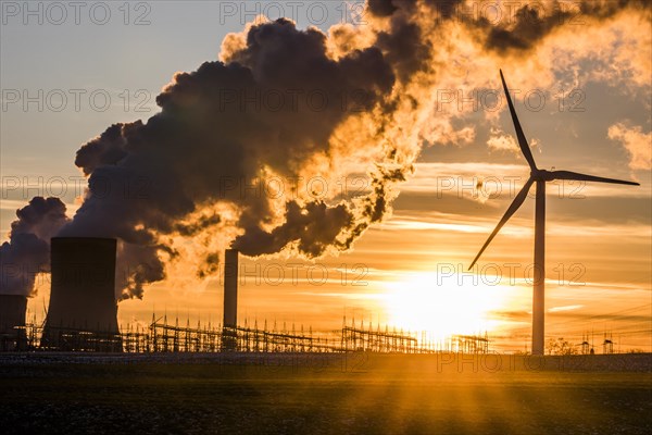 Wind turbine in front of steaming coal-fired power plant at sunset