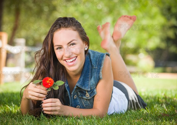 Attractive mixed race girl portrait laying in grass outdoors with flower