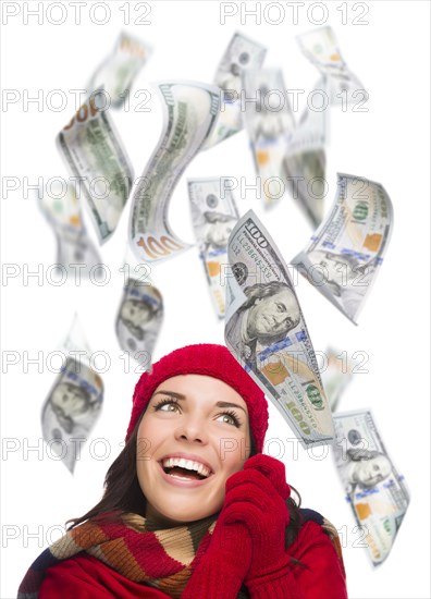 Young excited warmly dressed woman with $100 bills falling money around her on white