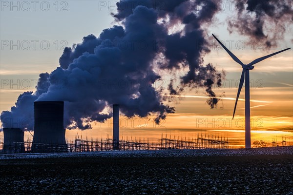 Wind turbine in front of steaming coal-fired power plant at sunset