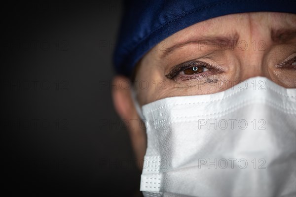 Tearful stressed female doctor or nurse wearing medical face mask on dark background