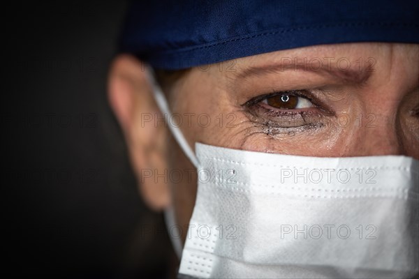 Tearful stressed female doctor or nurse wearing medical face mask on dark background