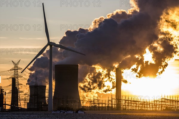 Wind turbine in front of steaming coal-fired power plant at sunset