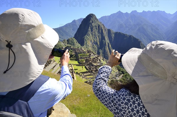 Tourists photograph the ruined city of the Incas and the mountain Huayna Picchu