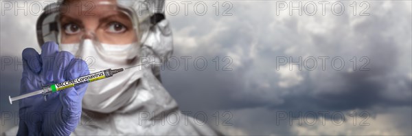 Doctor or nurse wearing surgical glove holding medical syringe with coronavirus COVID-19 vaccine label banner of clouds