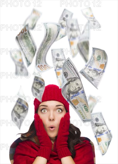 Young excited warmly dressed woman with $100 bills falling money around her on white