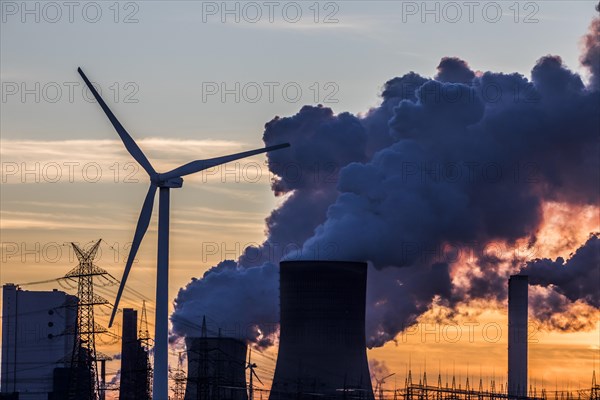 Wind turbine in front of steaming coal-fired power plant at sunset