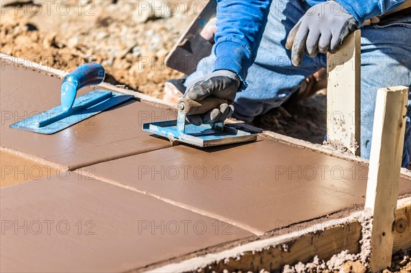 Construction worker using hand groover on wet cement forming coping around new pool