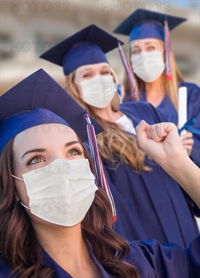 Several female graduates in cap and gown wearing medical face masks