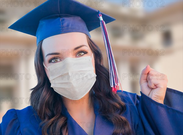 Female graduate in cap and gown wearing medical face mask