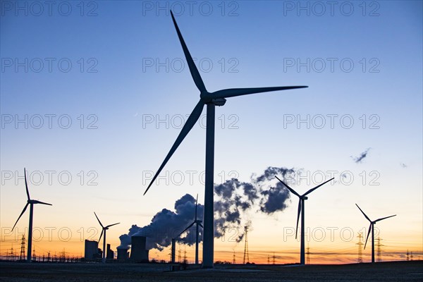 Wind turbines in front of steaming coal-fired power plant at sunset