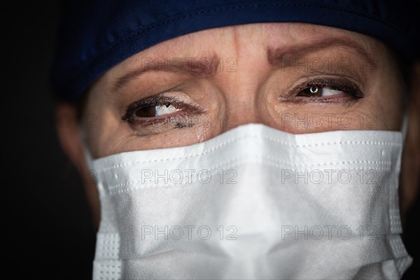 Tearful stressed female doctor or nurse wearing medical face mask on dark background