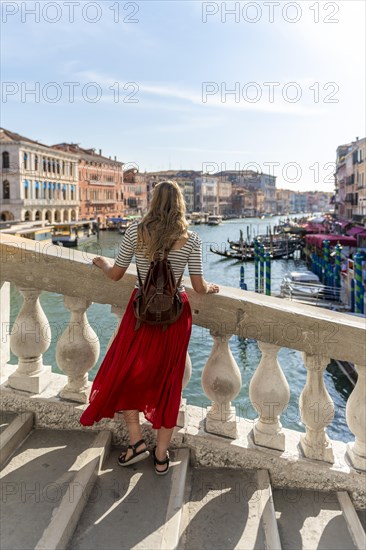 Young woman with red skirt walks over a bridge at the Grand Canal