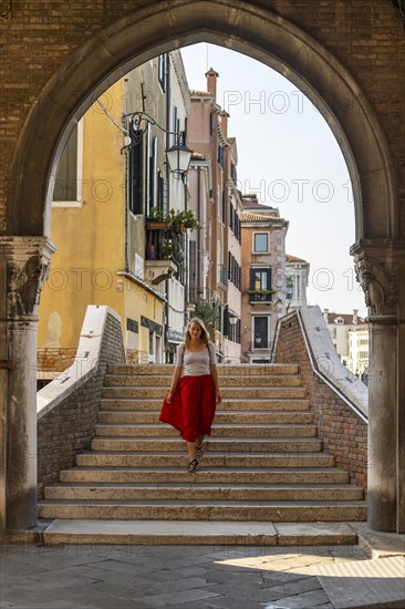 Young woman with red skirt walks through archway