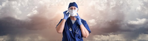 Doctor or nurse adjusting medical face mask wearing personal protective equipment over ominous clouds