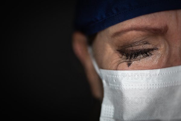 Tearful stressed female doctor or nurse wearing medical face mask on dark background